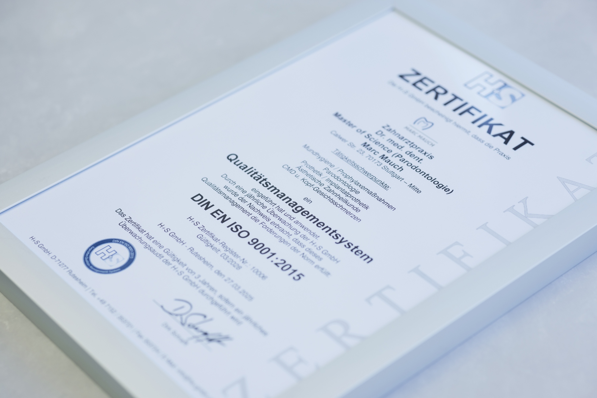 Zertifikat zur DIN EN ISO 9001:2015 Qualitätsmanagement-Zertifizierung in Rahmenansicht; schräg fotografiert auf heller Fläche.